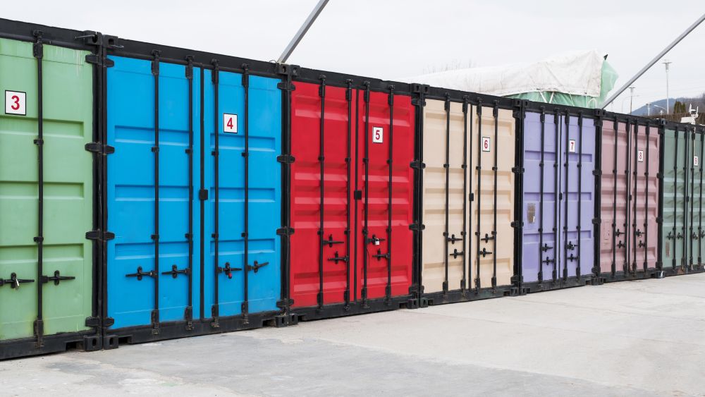 A row of colorful shipping containers, each with a number, lined up on a concrete surface under an overcast sky illustrates the variety of ISO container sizes and uses for businesses.